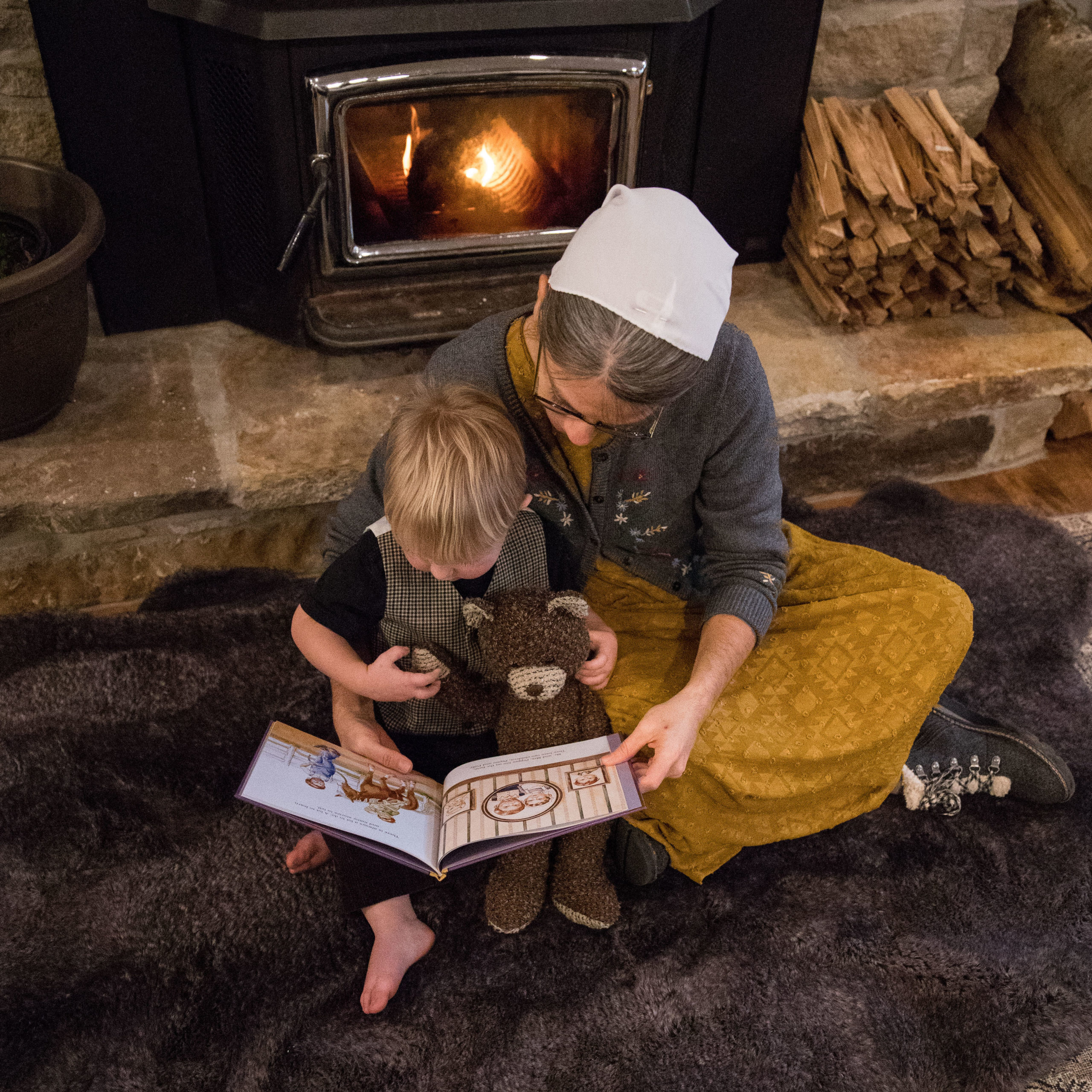 Lady reading to a small boy in front of the fire